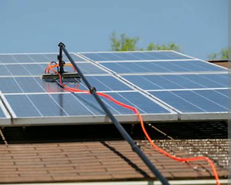 Telescopic water-fed pole with an orange hose cleaning panels on a residential roof